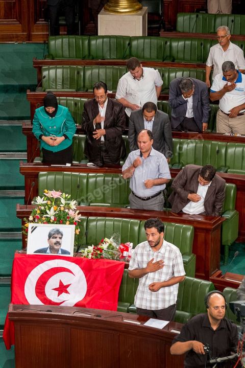 06 août 2013 : en place du siège du député assassiné  Mohamed Brahmi, des gerbes, son portrait et un drapeau national à la première séance de l'Assemblée depuis l'assassinat du député Mohamed Brahmi. La séance plénière débute par un long hommage au martyr avec prières et discours en présence des députés, hormis les 57 en retrait, du Premier Ministre et des ministres de l'Intérieur et de la Défense qui par leurs discours exposeront la situation dans le pays.