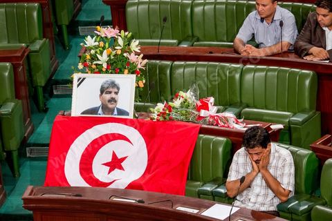 06 août 2013 : en place du siège du député assassiné  Mohamed Brahmi, des gerbes, son portrait et un drapeau national à la première séance de l'Assemblée depuis l'assassinat du député Mohamed Brahmi. La séance plénière débute par un long hommage au martyr avec prières et discours en présence des députés, hormis les 57 en retrait, du Premier Ministre et des ministres de l'Intérieur et de la Défense qui par leurs discours exposeront la situation dans le pays.