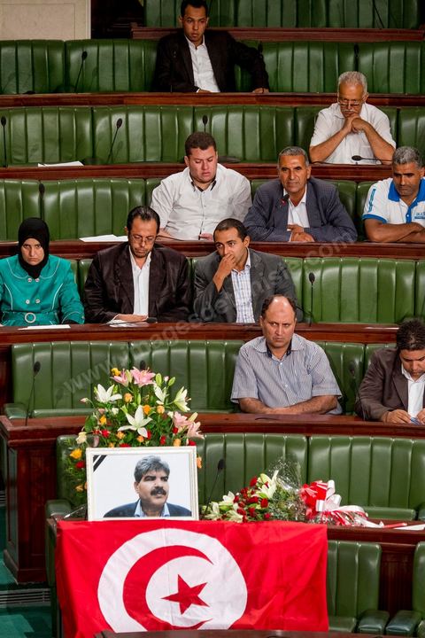 06 août 2013 : en place du siège du député assassiné  Mohamed Brahmi, des gerbes, son portrait et un drapeau national à la première séance de l'Assemblée depuis l'assassinat du député Mohamed Brahmi. La séance plénière débute par un long hommage au martyr avec prières et discours en présence des députés, hormis les 57 en retrait, du Premier Ministre et des ministres de l'Intérieur et de la Défense qui par leurs discours exposeront la situation dans le pays.