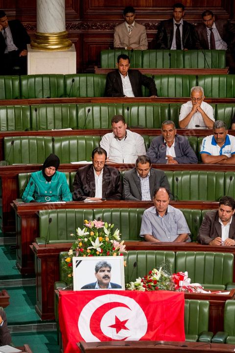 06 août 2013 : en place du siège du député assassiné  Mohamed Brahmi, des gerbes, son portrait et un drapeau national à la première séance de l'Assemblée depuis l'assassinat du député Mohamed Brahmi. La séance plénière débute par un long hommage au martyr avec prières et discours en présence des députés, hormis les 57 en retrait, du Premier Ministre et des ministres de l'Intérieur et de la Défense qui par leurs discours exposeront la situation dans le pays.