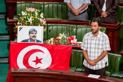 06 août 2013 : en place du siège du député assassiné  Mohamed Brahmi, des gerbes, son portrait et un drapeau national à la première séance de l'Assemblée depuis l'assassinat du député Mohamed Brahmi. La séance plénière débute par un long hommage au martyr avec prières et discours en présence des députés, hormis les 57 en retrait, du Premier Ministre et des ministres de l'Intérieur et de la Défense qui par leurs discours exposeront la situation dans le pays.