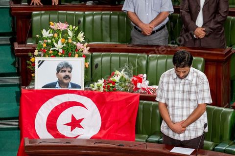 06 août 2013 : en place du siège du député assassiné  Mohamed Brahmi, des gerbes, son portrait et un drapeau national à la première séance de l'Assemblée depuis l'assassinat du député Mohamed Brahmi. La séance plénière débute par un long hommage au martyr avec prières et discours en présence des députés, hormis les 57 en retrait, du Premier Ministre et des ministres de l'Intérieur et de la Défense qui par leurs discours exposeront la situation dans le pays.