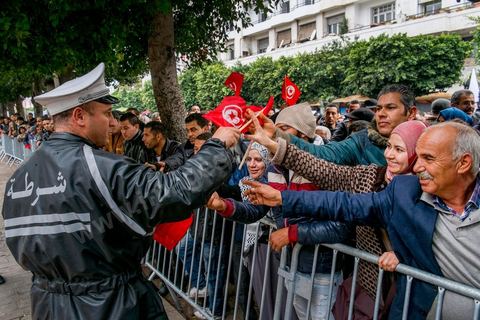 14 janvier 2014 : Un policier distribue des drapeau tunisien aux passants sur l'avenue Habib Bourguiba à Tunis quelques milliers de tunisiens sont venus se rassembler pour commémorer le troisième anniversaire du départ de l'ancien Président Ben Ali, aboutissement des mouvements de révoltes en région démarrés le 17 décmbre 2010. Tous les genres politiques se croisent et se chamaillent l'avenue, d'un côté les islamistes avec Ennahdha, les ligues et même un nouveau mouvement islamiste anachiste, de l'autre la gauche et l'opposition commémorant à la fois le départ des anciens et la mémoire des martyrs de la révolution et des martyrs politiques. 