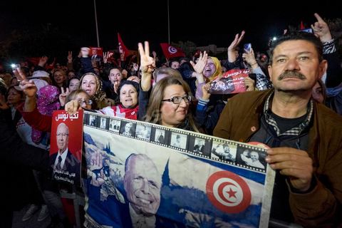 21 décembre 2014 : Militant avec portrait historique de Habib Bourguiba et de Béji Caid Essebsi. Dès la fin du scrutin à 18h, les rumeurs d'une large victoire de Beji Caïd Essebsi, candidat du parti Nidaa Tounes, circulent. Avec 8 à 10 points d'avance selon les sondages, Béji Caid Essebsi remporte les 1ères élections présidentielles libres en Tunisie depuis la révolution de 2011. A cette annonce les militants sont venus nombreux féter la victoire annoncée devant le QG de campagne du parti dans le quartier très huppé des Berges du Lac de Tunis.