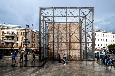 4 octobre 2017 : Dream City medina de Tunisie. Oeuvres de Nidhal Chamekh. Installation BARBED GATE : Au lendemain du 14 janvier 2011, les mesures de sécurité se sont renforcées dans la ville de Tunis. Ce qui était auparavant annoncé comme « mesures d’exception » s’est érigé en règle. Les fils barbelés et autres frontières font désormais partie du paysage urbain.Le choix d’intervenir sur Bab El Bhar correspond à la charge symbolique qu’elle a captée et les événements historiques qui l’ont façonnée tel un monument-frontière. Bab El Bhar est entièrement habillée en fil barbelé, confondant l’élément contrôlé et l’outil du contrôle. L’édifice imposant se retire au profit d’une silhouette fantomatique, remontant l’histoire d’une porte donnant sur la mer, rebaptisée Porte de France par les autorités coloniales et s’alignant aujourd’hui sur l’axe de la statue d’Ibn Khaldoun, celle de Bourguiba et l’Obélisque.