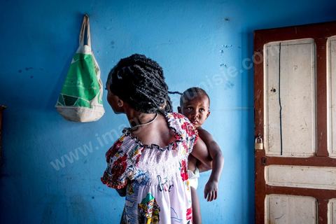 24 juin 2017 : Océane et son fils dans la cuisine. Chez Océane, migrante Ivoirienne à Tunis dans un quartier populaire. Elle vit dans une maison avec 2 chambres qu'elle partage avec son fils Eden et cinq autres ivoiriennes. Océane est arrivée en Tunisie en 2010 comme étudiante et est depuis 5 ans en situation irrégulière, ne lui permettant plus de travailler légalement. Il y a deux ans Eden est né, ce jeune garçon plein de joie est devenu sa raison de vivre, elle souhaite trouver un endroit pour vivre normalement et élever son fils. “J’estime que pour vivre bien Tunisie, il me faudrait entre 800 et 1000 dinars. Généralement, je suis plutôt à 350. Entre les couches et la nourriture, les dépenses sont rapides.” La jeune femme travaille de façon irrégulière : elle a quelques patrons qui l’appellent, selon leur besoin, pour faire le ménage chez eux. Une journée lui rapporte entre 25 et 30 dinars.  