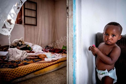 24 juin 2017 : Dans la chambre, Océane partage trois matelas posés au sol avec deux autres filles et deux bébés. Chez Océane, migrante Ivoirienne à Tunis dans un quartier populaire. Elle vit dans une maison avec 2 chambres qu'elle partage avec son fils Eden et cinq autres ivoiriennes. Océane est arrivée en Tunisie en 2010 comme étudiante et est depuis 5 ans en situation irrégulière, ne lui permettant plus de travailler légalement. Il y a deux ans Eden est né, ce jeune garçon plein de joie est devenu sa raison de vivre, elle souhaite trouver un endroit pour vivre normalement et élever son fils. “J’estime que pour vivre bien Tunisie, il me faudrait entre 800 et 1000 dinars. Généralement, je suis plutôt à 350. Entre les couches et la nourriture, les dépenses sont rapides.” La jeune femme travaille de façon irrégulière : elle a quelques patrons qui l’appellent, selon leur besoin, pour faire le ménage chez eux. Une journée lui rapporte entre 25 et 30 dinars.  