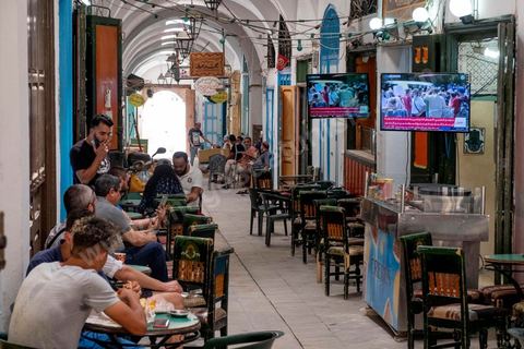 26 juillet 2021 : dans le souk des chéhias, accolé au Premier ministère, les gens continuent leurs activités tout en regardant en live les événements du Bardo. Au lendemain de l'annonce du limogeage du chef du gouvernement par le Président Kais Saeid dans le cadre de son "coup d'état" constitutionnel, la place de la Kasbah à Tunis, centre du pouvoir exécutif, avec le Premier ministère, le ministère des finances et de la Défense, est bouclée, vidée de ses fonctionnaires interdits par l'armée de retourner ce matin à leurs postes. En cette fin de journée, Kais Saied, qui détient désormais tous les pouvoirs, a annoncé une fermeture administrative complète dans le pays pour deux jours. 