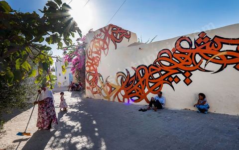 Oeuvres de l'artiste tunisien EL SEED pour le Projet DjerbaHood : après la Tour Paris 13, la team Itinerrance dépose ses valises dans un village traditionnel de l’île de Djerba, Erriadh. Depuis le début du mois de juillet, le village d’Erriadh se métamorphose petit à petit pour devenir un véritable musée à ciel ouvert. Une sélection d’artistes des quatre coins du monde ont été invités à s’exprimer dans ce décor unique à l’architecture authentique : murs blancs, portes bleues turquoises, dômes, veilles constructions et divers lieux abandonnés, autant de possibilités qui donneront naissance à des créations uniques aux couleurs locales.