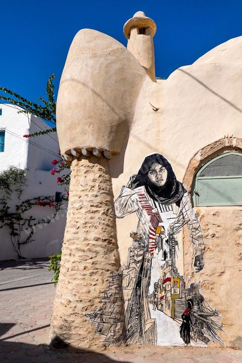 Oeuvres de l'artiste américain SWOON pour le Projet DjerbaHood : après la Tour Paris 13, la team Itinerrance dépose ses valises dans un village traditionnel de l’île de Djerba, Erriadh. Depuis le début du mois de juillet, le village d’Erriadh se métamorphose petit à petit pour devenir un véritable musée à ciel ouvert. Une sélection d’artistes des quatre coins du monde ont été invités à s’exprimer dans ce décor unique à l’architecture authentique : murs blancs, portes bleues turquoises, dômes, veilles constructions et divers lieux abandonnés, autant de possibilités qui donneront naissance à des créations uniques aux couleurs locales.