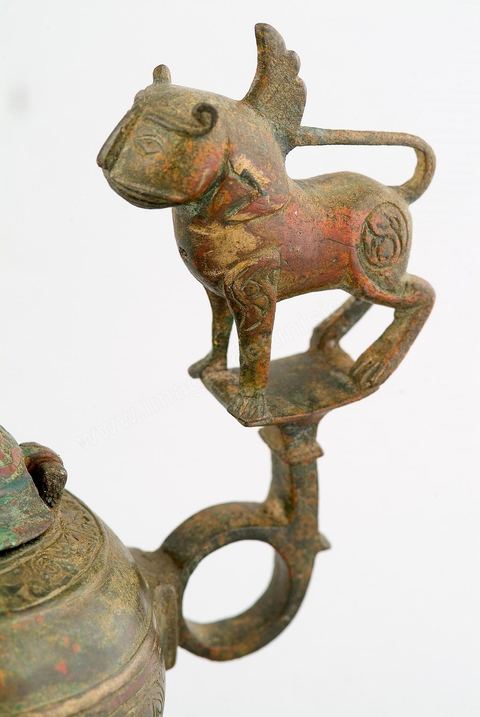 LAMPE À HUILE AU LION AILÉ.Khorassan, 12  siècle.La représentation du merveilleux puise sa source dans les croyances de l'Arabie pré-islamique, les mythes de l'Antiquité Classique et iranienne auxquels se sont greffés les apports de l'Asie Centrale et la fascination qu'exerçaient les récits de voyage. Phénix, harpie, griffon, pégase, dragon, waq-waq (arbre à figures humaines) ornaient objets, textiles et manuscrits. Le sphinx, un lion à figure humaine, avec ou sans ailes, y prenait une bonne place. Les lampes à huile en métal sont, le plus souvent, munies d'une figure d'oiseau rehaussant le poucier.Sur cette vigoureuse lampe à huile, les ailes, symbole de lumière et de survie, le lion, symbole de majesté et de maîtrise, s'associent, en ronde-bosse, pour conférer à la lampe une sorte de valeur 'magique', évoquant force et éternité. - Musée Lella Hadria à Djerba Explore
