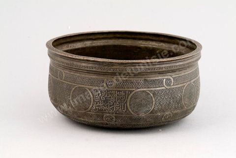 BASSIN EN CUIVRE ÉTAMÉ. Egypte/Syrie, 15 - 16  siècle.À l'heure de la chute de la dynastie mamelouke (1258-1512) et de l'annexion de la Syrie et de l'Egypte à l'Empire ottoman, le manque de métal précieux incita les artisans à enrichir les surfaces des pièces de décors ciselés très denses. Ils devaient couvrir, comme sur ce bassin, jusqu'aux parties les moins visibles, tel que le fond extérieur. L'étamage qui couvre la couleur cuivrée et l'incrustation d'une pâte bitumineuse noire, devaient apporter les effets d'éclat et de contraste, obtenus habituellement par l'argent. - Musée Lella Hadria à Djerba Explore