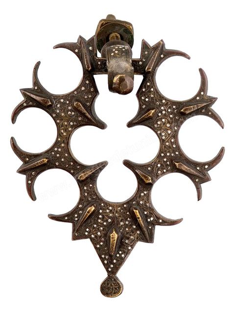 HEURTOIR EN BRONZE INCRUSTÉ D'ARGENT. Egypte/Syrie, fin de l'époque mamelouke, 15  siècle.Bronze coulé, décor gravé, maté et incrusté d'argent. Décor de rinceaux fleuris. La découpe s'inspire d' un motif floral.  Les quatorzes amandes ou gouttes, en relief, connues depuis longtemps dans le bronze du Khorassan, seraient des boutons de lotus. À la suite de l'invasion mongole et la chute de Bagdad (1258), le califat abbaside fut transféré au Caire, inaugurant lerègne des Sultans Ayyubides (1171-1250) suivi par les mamelouk jusqu'en 1517. Les grands artisans d'Irak, se sont alors mis au service des nouveaux princes de Syrie et d'Egypte. L'art du métal et les applications du métal ouvragé sur les portes prospèrent particulièrement  au Caire, avec une prédilection pour les motifs géométriques, floraux ou graphiques. Certains exemplaires seront entièrement couverts de calligraphie (voir salle suivante). Caractéristiques de la manière mamelouke, monumentale et quelque peu ostentatoire, de splendides heurtoirs, venaient orner les portails des fondations royales.Une pièce, similaire à celle-ci, est conservée au Musée du Louvre à Paris, munie de sa plaque de fond. - Musée Lella Hadria à Djerba Explore