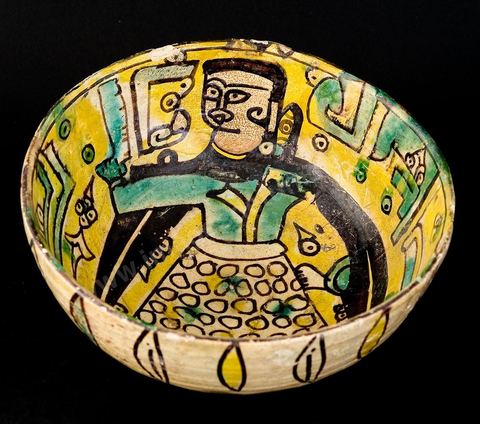 COUPE DE LA DAME EN CAPE NOIREKhorassan, Nichapour, 10 - 11  siècleUn personnage féminin en vêtement ocellé et cape noire à fausses manches pointues, tient à  la main un objet difficile à identifier (hache, miroir ou parchemin).Le thème de la dame debout, à l'oeil étiré (mais vu de profil), tenant un objet, se rencontre dans la céramique 'tunisienne' du 10 siècle. C'est le décor central ornant deux plats dits Dame de Sabra, découverts sur le site fatimide de Sabra Mansouriya et conservés au Musée des Arts Islamiques à Raqqada (Kairouan).