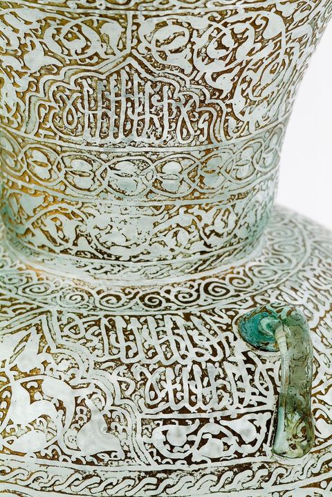 LAMPE DE MOSQUÉE EN VERRE GRAVÉ ET DORÉ.Syrie ottomane, 19  siècle.Cette lampe de mosquée à trois anses, à panse globulaire et haut col évasé reproduit un modèle classique  connu en Egypte ou en Syrie durant la période mamelouke (14 siècle). La même forme caractérise une poterie du 10 siècle, trouvée à Raqqada en Ifrikya (Tunisie). Elle inspirera les céramistes d'Iznik en Turquie (16 siècle) et plus tard les verriers d'Europe et de Syrie (19 siècle).À haute valeur symbolique, on la retrouve reproduite dans les portières de mosquée, les tapis de prière de Perse ou d'Anatolie où elle suggère un renvoi à un célèbre passage du Coran. Chapitre de La Lumière V.35. Voir tapis adjacent.