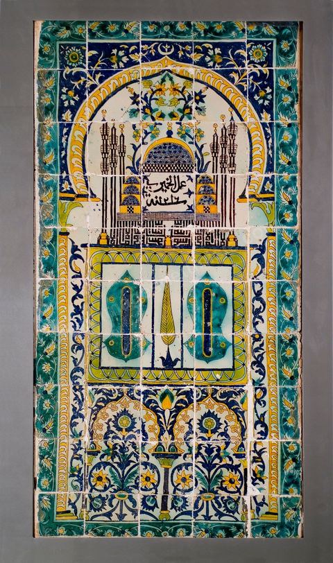 PANNEAU DE CÉRAMIQUE AUX SANDALES DU PROPHÈTE.Tunisie, husseïnide, signé et daté, Khémiri 1216 H./1801Panneau à thème de 'mihrâb', la niche de prière en Islam. Le cadre est orné de rinceaux fleuris de 'lotus' et de feuilles de 'SAZ' ottomanes. Au centre de l'arc, on reconnaît une mosquée à coupole centrale de style ottoman. Six minarets s'élancent, traçant, en graphie coufique à haute hampe, et en miroir, la profession de foi musulmane: Il n'y a de Dieu qu'Allah et Mohammad est son prophète". À leur base se dessine une minuscule porte jaune à claveaux bruns et blancs, donnant une idée de la proportion suggérée. Au centre du mihrâb, de part et d'autre d'une palme, un panneau figurant les sandales du prophète. Au dessous, deux arcs polylobés renfermant une composition florale. La croyance dans les vertus bénéfiques, la baraka, des attributs corporels et vestimentaires du prophète, est encore de nos jours, vivante en Islam. Une sorte de culte est voué à l'empreinte de son pied conservée à Istanbul, et à trois de ses cheveux, enterrés au mausolée de son compagnon, Abou Zamaâ Al Balaoui, à Kairouan, quatrième ville sainte de l'Islam. Du Maroc jusqu'en Inde, les Sandales du prophète ont une place particulièrement éminente, ornant ici les enluminures, là, donnant leur nom à une mosquée. Dans les lieux où elles figurent, elles évoquent la 'visite' ou la 'présence' du prophète. Leur aura assure au lieu protection et patronage. Les cinq motifs en oeilletons, au nombre des doigts de la main, qui ponctuent les sandales, contribuent à la protection et à l'éloignement du mauvais oeil.  La signature de l'artiste, peu courante dans ce genre d'ouvrage et dans l'art  arabe en général, prend, au dessous de la grande coupole, une position centrale, immodeste. Un voeu de piété, le désir d'être enterré auprès du prophète - la mosquée serait celle de son mausolée à Médine -, pourrait la justifier. Protecteur de la demeure 