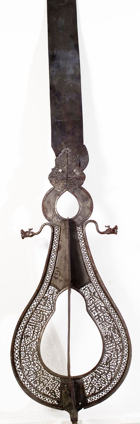 ÉTENDARD DE CÉRÉMONIE RELIGIEUSE. Perse, safavide,  daté de 1658 - 1659, mis en main-morte en 1696-7Acier décoré en ajour où s'inscrit en plein un extrait de la Sourate 48, verset 4, du Coran:  'Lui qui fait descendre la sérénité au coeur des croyants pour que, déjà croyants, ils grandissent dans la croyance.' 'À Dieu armées des cieux et de la terre et Dieu est connaissant et Sage '.L'exégèse relie ce passage du Coran tiré du Chapitre Al Fath, 'le Succès' ou 'la Conquête', à une bataille menée par le prophète Mohammad contre les païens au sujet, semble-t-il, de la prise de la Mecque. Prêts à se déployer, gueules ouvertes et dents acérées, deux dragons veillent à la protection de l'étendard. D'origine chinoise le thème du dragon, connu dans les cultures turques, était très en vogue en Perse durant la période safavide (16  - 18  siècle). La Porte dite du 'Talisman' à Bagdad, disparue aujourd'hui, était déjà ornée d'un impressionnant couple de dragons, symbole de majesté et de protection. (13 siècle)