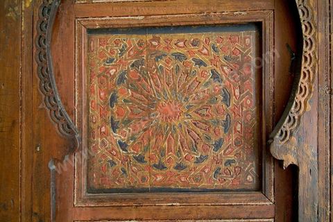 DOUBLE-PORTE À DÉCOR ÉTOILÉ. Maroc, 18   siècle.L'abondance du bois au Maroc, rare dans les pays arabes, a permis la généralisation de son usage en architecture.Toujours ouvragés, souvent peints, poutres, solives, corbeaux, linteaux, piliers, frises et portes se multiplient autant en intérieur qu'en extérieur. Il est dans les pièces, les patios, les façades et dans les passages couverts des ruelles et impasses. Une sculpture particulièrement riche en étoiles et arabesques caractérisaient les mosaïques de bois de l'époque mérinide. La porte exposée ici en hérite la composition étoilée mais réduite à un léger relief. Ses fonds sont décorés de polygones fleuris d'inspiration orientale. D'un effet particulièrement spectaculaire, dans les patios ou les jardins intérieurs des palais et riadh marocains, ce genre de double-porte donne accès à la salle de réception. Elle est souvent couronnée, d'une paire de corbeaux, en pavillon miniature, ornés ici de niches renfermant une fleur d'oeillet. Répondant aux crapaudines inférieurs aménagées dans le marbre, les goujons supérieurs venaient évoluer à l'intérieur de ses corbeaux, préalablement scellés au mur. Durant la saison froide, on se contentait d'ouvrir les portes basses.