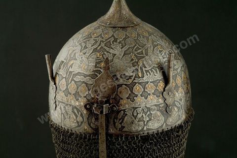 CASQUE DE CÉRÉMONIE.Perse qâdjâre,19  siècle.Acier, Or et Argent.Cette forme, en pointe, est archaïsante et se retrouve dans de nombreuses miniatures à thème guerrier. Le repertoire iconographique, scène de chasse à courre, où abondent les figures humaines et animalières, permet de situer le casque dans la série des armures à usage cérémonial, caractéristique des rites chîîtes. Apporté, vraisemblablement, par les turcs, ce genre de casque se retrouvait en Tunisie. Un casque dit, 'de Rostam' est conservé au Musée Militaire du Palais de la Rose, dans la banlieue de Tunis.	 - Musée Lella Hadria à Djerba Explore