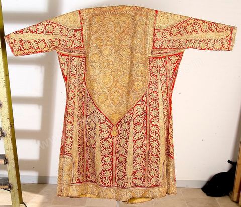 CAFETAN AUX CYPRÈSPerse/Asie Centrale, 19  siècle.Composition très dense caractéristique des costumes d'Asie Centrale. Décors de cyprès et de rinceaux fleuris en fil d'or et d'argent sur fond de soie rouge.Un type de cafetan comparable aurait été porté à Alger durant la période ottomane.