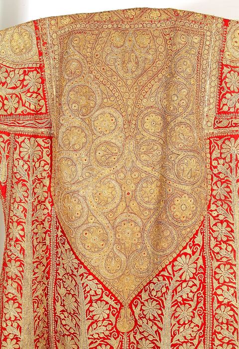 CAFETAN AUX CYPRÈSPerse/Asie Centrale, 19  siècle.Composition très dense caractéristique des costumes d'Asie Centrale. Décors de cyprès et de rinceaux fleuris en fil d'or et d'argent sur fond de soie rouge.Un type de cafetan comparable aurait été porté à Alger durant la période ottomane.