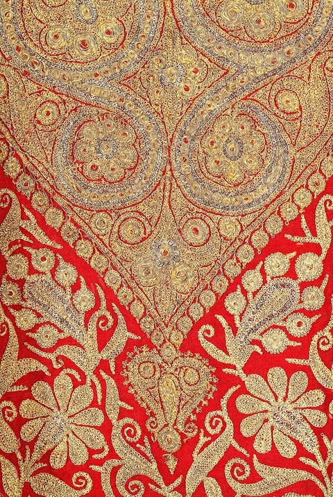 CAFETAN AUX CYPRÈSPerse/Asie Centrale, 19  siècle.Composition très dense caractéristique des costumes d'Asie Centrale. Décors de cyprès et de rinceaux fleuris en fil d'or et d'argent sur fond de soie rouge.Un type de cafetan comparable aurait été porté à Alger durant la période ottomane.