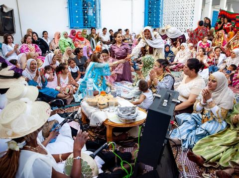 Lors d'un mariage traditionnel à Djerba, la soirée des femmes rassemble la communauté autour de la mariée, parée de la haajba, la tenue nuptiale djerbienne aux ornements précieux transmise de génération en génération. La musique est portée par des chanteuses et musiciens noirs, descendants des communautés subsahariennes établies sur l'île, qui animent la fête au son de la darbouka et du tambour, dans une tradition musicale propre au mariage djerbien.