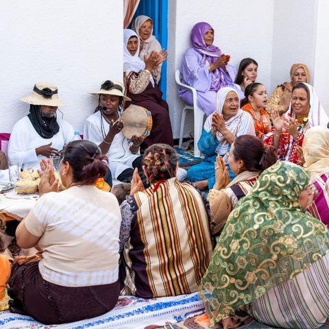 Lors d'un mariage traditionnel à Djerba, la soirée des femmes rassemble la communauté autour de la mariée, parée de la haajba, la tenue nuptiale djerbienne aux ornements précieux transmise de génération en génération. La musique est portée par des chanteuses et musiciens noirs, descendants des communautés subsahariennes établies sur l'île, qui animent la fête au son de la darbouka et du tambour, dans une tradition musicale propre au mariage djerbien.