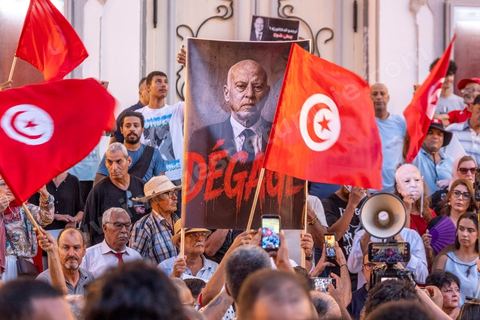 Tunis, Tunisia – August 20, 2026. Protesters march through downtown Tunis against President Kaïs Saïed, calling for his resignation and demanding greater political freedoms and the release of detainees and opposition figures. Portraits of the president crossed out with the slogan “GET OUT,” Tunisian flags, and signs accompany the protest. The protest comes amid growing social discontent following several weeks of extreme heat, water and power outages, and difficulties in accessing certain medications and essential goods.
