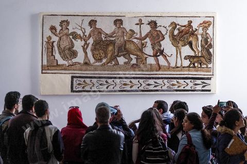 Mosaïque de la Procession Dionysiaque, milieu du IIème siècle après JC. Le musée archéologique de El Djem, cité antique de Thysdrus, a été aménagé à l’emplacement d’une villa romaine dont il restitue l’organisation spatiale : une cour centrale entourée d’un péristyle – préau – qui donne accès aux chambres. Là, sont exposés des objets – sculptures, tableaux en mosaïque, céramique, etc. – provenant de campagnes de fouilles menées à Thysdrus aussi bien que dans les environs de la cité.