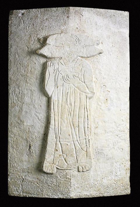 Ossuaire en calcaire à couvercle orné d'un personnage en relief plat portant une barbe et des vétements, la main droite est levée dans un geste de prière et la gauche tient une coupe, sa tête repose sur deux gros coussins. (nécropole de rabs, Carthage, IIIème siècle avant JC, musée de Carthage).