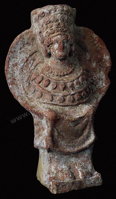 Déesse assise en terre cuite, le buste entouré d'un voile circulaire et coiffée d'un immense diadème. Elle porte de longues boucles d'oreilles et un lourd pectoral formé de colliers lui couvre la poitrine. Cette surabondance ornementale semble avoir une valeur symbolique (H. 18 cm, nécropole punique de Byrsa, IVème siècle avant JC, musée de Carthage).