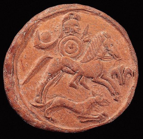 Médaillon en terre cuite représentant un guerrier montant sans selle un cheval au galop. Coiffé d'un casque à cimier et armé d'un bouclier rond et d'une lance, il est accompagné d'un chien. Devnat le cheval figure une fleur de Lotus ou de Lys, et derrière le cavalier sont représentés un croissant et un disque solaire. Il pourrait s'agir d'une divinité guerrière (diam. 9 cm, nécropole deDouimès, Carthage, VIème siècle avant JC, musée de Carthage).