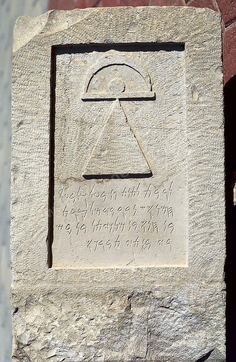 Stèle votive en calcaire grisâtre qui se distingue de la plupart des autres stèles par sa forme rectangulaire, sa présentation, l'absence de fronton et d'acrotères ainsi que de tout autre décor en dehors du signe dit de Tanit, qui n'est pas incisé mais sculpté en bas relief. On retrouve certes le triangle avec le cercle posé sur sa point mais la barre qui le surmonte se termine en demi-cercle, évoquant le croissant, au lieu de prendre une forme anthropomorphe, assez fréquente, par l'adjonction de bras relié. La dédicace est en l'honneur de Tanit et de son parèdre le seigneur Baal Hammon. Cette stèle confirme la prédilection des Puniques pour les figures géométriques et les images symboliques : le signe dit de Tanit a l'apparence de l' "ankh" égyptien et son sens vital. Bien que l'on possède plus de 7000 stèles (dont 1000 au musée du Louvre) et plus de 6000 dédicaces, les représentations de Tanit et de Baal Hammon par d'autres moyens que leurs symboles sont rarissimes (H. 59 cm, l. 33,5 cm, tophet, Carthage, IVème siècle avant JC, musée de Carthage.