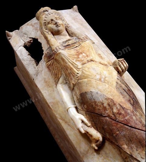 Sarcophage dit de la prêtresse en marbre blanc, orné en haut-relief d'un personnage féminin. Elle porte une longue robe plissée enserrée vers le bas par deux grandes ailes croisées. Un voile surmonté d'une tête de faucon lui couvre la tête à la manière du Klaft. Elle tient dans la main droite une colombe et gauche un vase à encens (H. 93 cm, L. 193 cm, l. 67 cm, nécropole de Sainte Monique, Carthage, IIIème siècle avant JC, musée de Carthage.