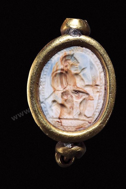 Scarabée en pierre d’un gris bleuté serti d’or, représentant un guerrier agenouillé portant casque, lance et bouclier ( Utique, IVe siècle av. J.-C., musée du Bardo ). section punique - musée du bardo