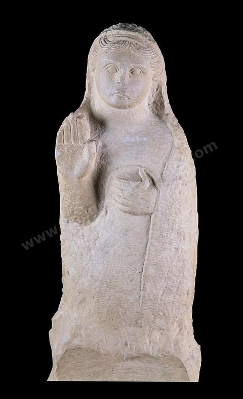 Stèle funéraire en forme de statue figurant un personnage féminin debout sur un piédestal. Un voile posé sur l’arrière de la tête enveloppe presque tout le corps‑; la chevelure soigneusement dessinée dénote une influence grecque archaïque. La main droite est levée en signe de prière, la gauche tient une pyxide. Cette stèle était érigée au-dessus du puits funéraire d’une tombe de Carthage ( H. 73,5‑cm, nécropole de Borj Jedid, Carthage, IVe-IIIe siècles av. J.-C., musée du Bardo ).scetion punique - musée du Bardo